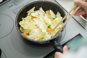 野菜炒めを作る若い女性　料理イメージ