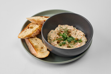 Rillettes of smoked salmon and cream cheese in a bowl with a baguette on a gray background
