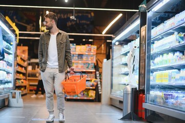 Young man buying groceries at the supermarket. Other customers in background. Consumerism concept.