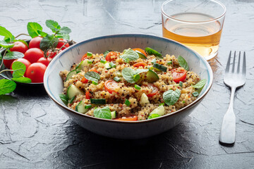 Quinoa tabbouleh salad in a bowl, a healthy dinner with tomatoes and mint, on a black slate background