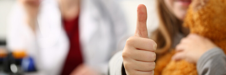 Little girl holding thumbs up in doctor office. Recommending quality healthcare services for...