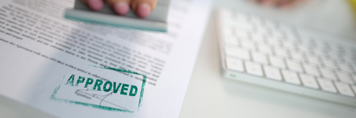 Closeup of a person hand stamping green approved seal on text approved document on table. Contract form and business agreement with partner