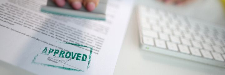 Closeup of a person hand stamping green approved seal on text approved document on table. Contract...