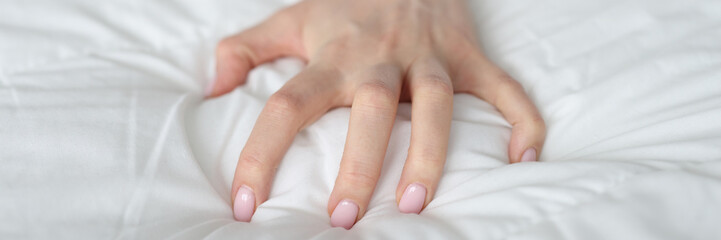 Strongly clenched female hand on sheet on bed. Intimacy of young woman on bed or bad dream concept