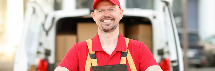 Smiling courier stands in front of van with parcel. Logistics and parcel delivery concept