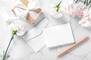 Blank card and envelop with pen, flowers and gift box on marble background