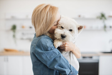 Close up view of tender young woman cuddling little white dog while holding clever pet in arms...