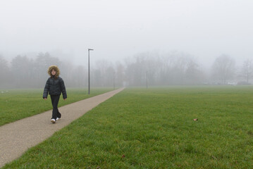 A girl in a foggy park walks along a path
