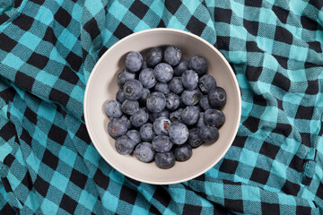 Ripe blueberry in a bowl on a plaid blanket top view