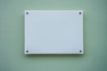White glass nameplate on spacer metal holders mounted on office building wall outside. Clear printing board for branding with mockup space.