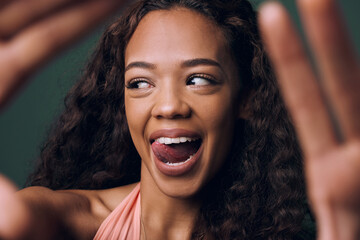 Selfie, tongue out and happy gen z girl with natural beauty, hair or smile on green background. Face, emoji and female influencer with fun, quirky or silly in studio for profile picture or blog - obrazy, fototapety, plakaty