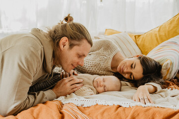 Young mother and father with their little daughter hugging and kissing on the bed.