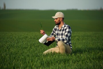 Naklejka na ściany i meble In checkered shirt and with notepad. Handsome young man is on agricultural field