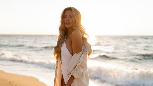 Beautiful blond woman in sexy swimwear posing on the beach in sunset light. Prtfect wavy hairs, tan skim body. Summer tropical mood.