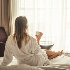 Woman in white bathrobe lying on sofa and relaxing with cup of tea at home.