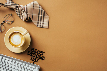 Happy Father's Day concept. Flat lay composition with mug of coffee, keyboard, necktie, glasses, message Happy Fathers Day on brown table. Top view, overhead.