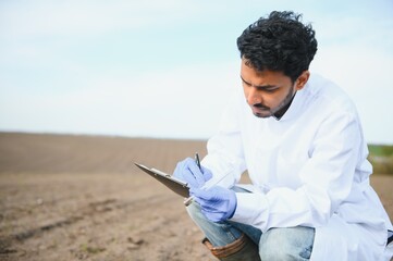 Soil Testing. Indian Agronomy Specialist taking soil sample for fertility analysis. Hands in gloves...