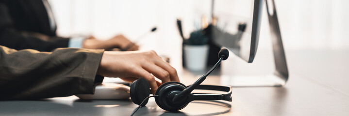 Panorama focus hand holding headset on call center workspace desk with blur background of operator...
