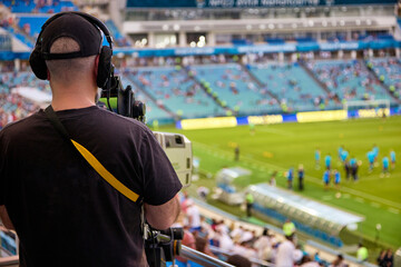 Professional cameraman in a black T-shirt with a camera shoots a football match in the stadium....