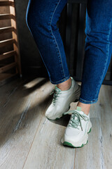 White leather summer sneakers on female legs in jeans. Women's casual sneakers. Comfortable women's shoes
