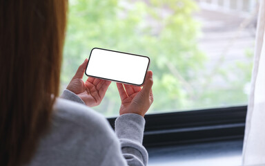 Mockup image of a woman holding and using mobile phone with blank desktop white screen at home
