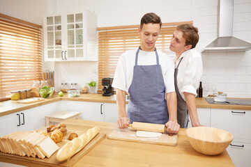 LGBT gay couple making a bread together in the kitchen - obrazy, fototapety, plakaty