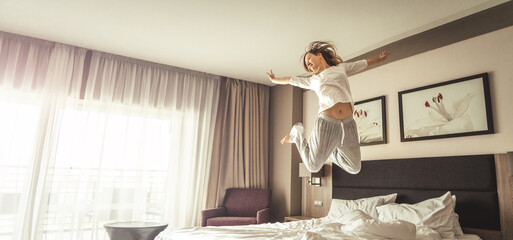 Woman having fun and jumping with bathrobe on bed in hotel room