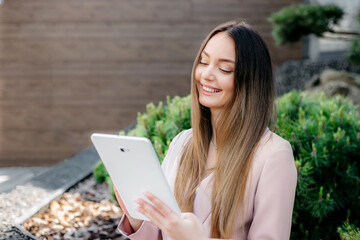 Fototapeta premium smiling caucasian office employee looking at tablet screen and sitting outdoors
