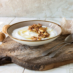 a bowl of greek yogurt with walnuts and honey on a light table