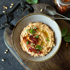 bowl of hummus with basil and sundried tomatoes on the table - obrazy, fototapety, plakaty