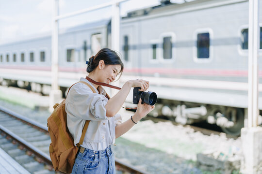 Asian teenage girl traveling using a camera take a photo to capture memories while waiting for a train at the station.