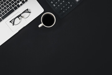 Flat lay black background with laptop, coffee cup and calculator, top view.