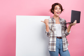 Portrait of charming astonished girl hold netbook direct finger empty space promo poster isolated...