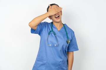 Beautiful doctor woman standing over white studio background smiling and laughing with hand on face covering eyes for surprise. Blind concept.