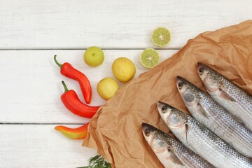 Fresh mullet fish on paper, on a white wooden table with ingredients for cooking.  Top view with copy space.