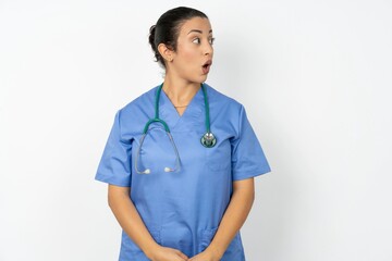 Shocked Beautiful doctor woman standing over white studio background look empty space with open mouth screaming: Oh My God! I can't believe this.