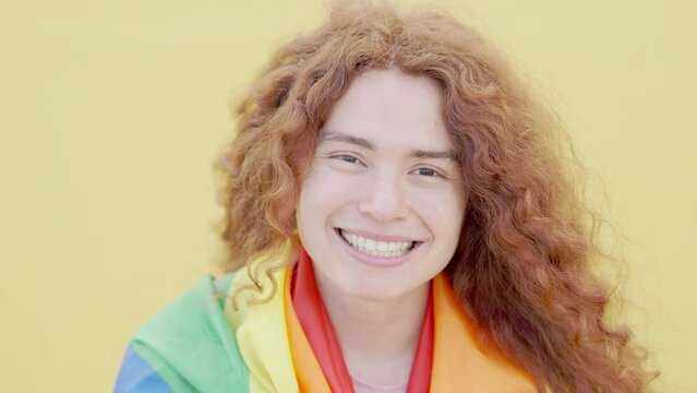Headshot portrait video of gay woman looking at camera - Happy non binary female holding rainbow flag smiling outdoors - Gay pride and lgbtq community concept	