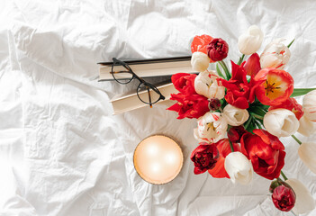 Spring background with a bouquet of tulips, a candle and books in a white bed.