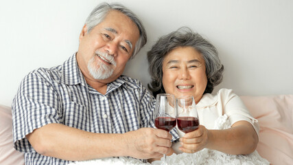 Happy love Elderly couple smile holding a wine glass , Senior couple old man and senior woman relaxing On the bed in the bedroom Celebrate the wedding anniversary - lifestyle senior concept