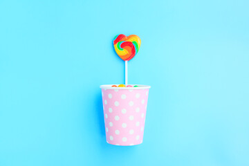 Colorful lollipop out of a pink paper cup with white dot on blue background, Colorful sweet lollipop