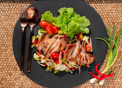 Grilled pork with fresh vegetable salad on a black plate. Close up