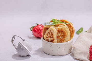 Cottage cheese pancakes, syrniki, curd fritters with strawberry, mint and powdered sugar in a bowl