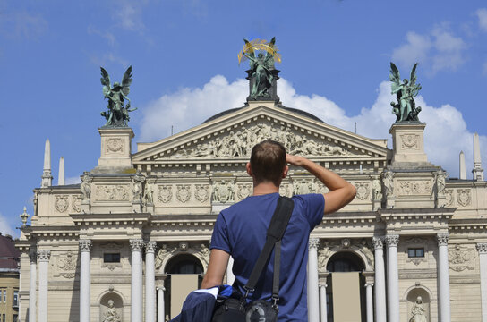 A male tourist looks at the beautiful facade of the building. Sunlight. Lviv Opera and Ballet Theater is out of focus. View from the back