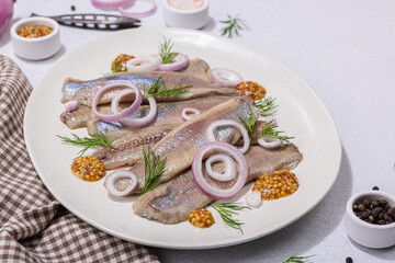 Salted herring with dijon mustard, dill and red onion rings on white stone background