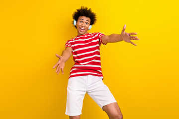 Photo of cheerful impressed guy wear striped t-shirt earphones having fun isolated yellow color background