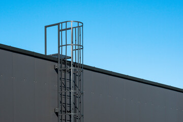 Steel ladder are on the side of the grey industrial building wall - obrazy, fototapety, plakaty