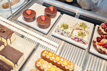 A variety of cakes covered with chocolate and decorated with pistachio mousse. A showcase in a pastry shop with delicious desserts with fresh berries and cream. Delicious pastries in the coffee shop