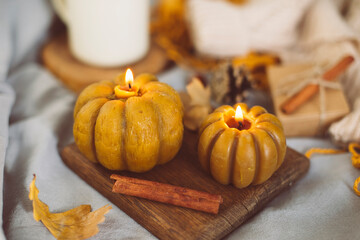 Burning candles shape of pumpkin and autumn decor on bed in bedroom