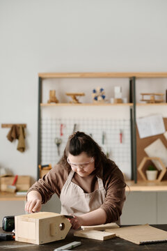 Vertical image of girl with down syndrome in protective glasses making birdhouse in workshop