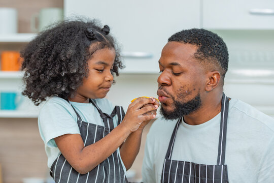 african afro hair black kid Cute taste oranges citrus sour flavour on lips mouth with daddy in kitchen. back african daughter kid afro hair and daddy frowning face for taste is sour of sliced orange